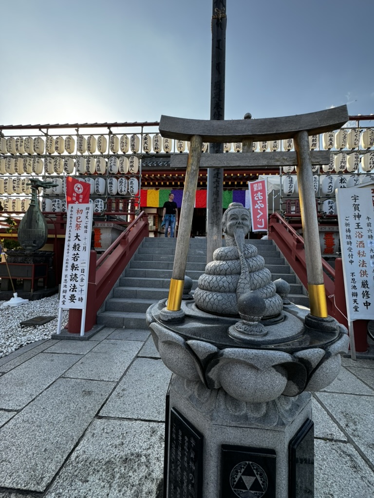 Views outside of a shinto shrine in Tokyo show a statue and archways with traditional paper lanterns in the background